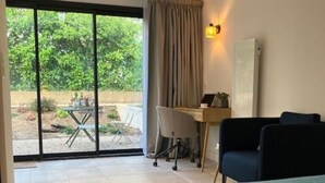 A bedroom with a bed, a desk, and a chair. There is a sliding glass door leading to a patio with a table and chairs. - Quiet studio in a green setting (Charbonnières-les-Bains)