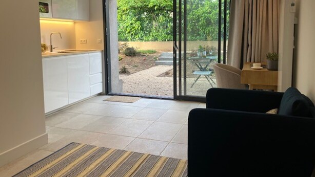 A modern living room with a sofa and a dining area with a table and chairs. A sliding glass door leads to a garden with a table and chairs. - Quiet studio in a green setting (Charbonnières-les-Bains)