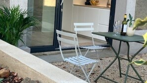 A modern outdoor seating area with a table and chairs, a bottle of wine, and a potted plant. - Quiet studio in a green setting (Charbonnières-les-Bains)