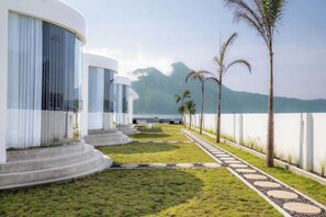 A modern resort with a curved building, a well-maintained lawn, and a clear view of the mountains. - Intan Lake View Kintamani (Bali)