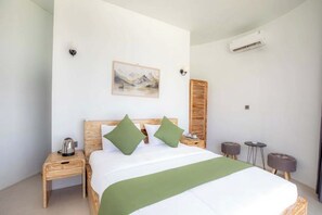A neatly arranged bedroom with a bed, a bedside table with a kettle, a wall-mounted air conditioner, and a small table with two stools. - Intan Lake View Kintamani (Bali)
