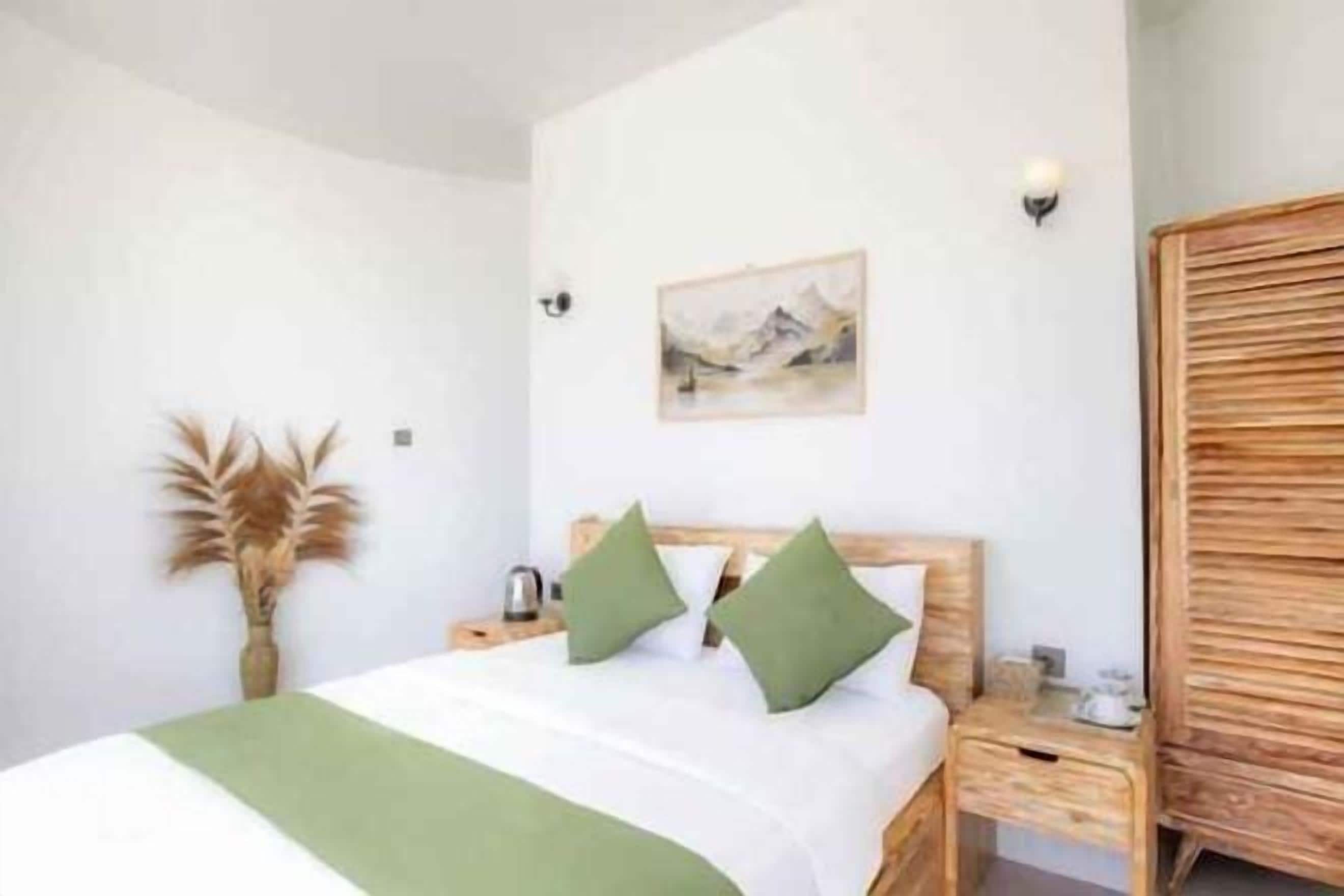 A bedroom with a bed, bedside tables, a nightstand, a lamp, a painting, and a wardrobe.