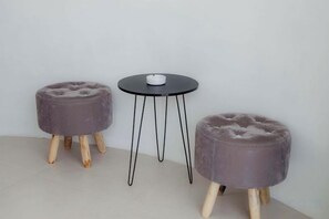 Two round ottomans with wooden legs and a small round table with a white object on it, against a plain wall. - Intan Lake View Kintamani (Bali)
