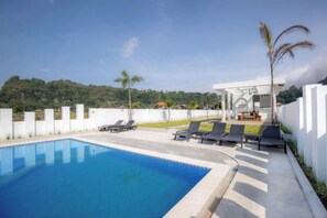 Μια πισίνα με ξαπλώστρες, μια σκεπαστή περιοχή με καθίσματα και θέα σε ένα καταπράσινο τοπίο.