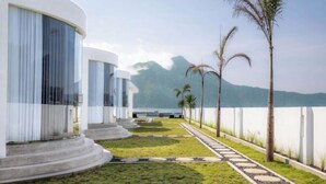 Un resort moderno con un camino que lleva a una piscina, rodeado de palmeras y vistas a las montañas.