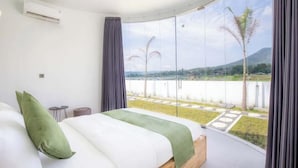 Un dormitorio con una cama grande, vistas a un jardín, y un balcón con vistas a un lago y montañas.