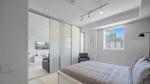 A modern bedroom with a bed, a chair, a desk, and a large window. - Beachside Charm: Walk to the Beach (Miami Beach)