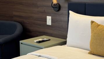 A neatly made bed with a white and gold pillow, a bedside table with a remote control, and a wall-mounted lamp.
