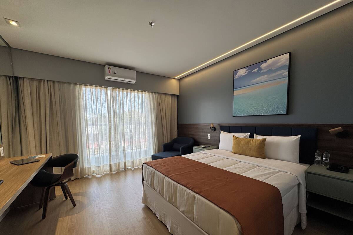 Una camera d'albergo con un letto, una scrivania, una sedia, un comodino e un quadro appeso al muro.