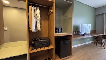 A hotel room with a wooden wardrobe, a desk with a computer, a TV, and a small refrigerator.