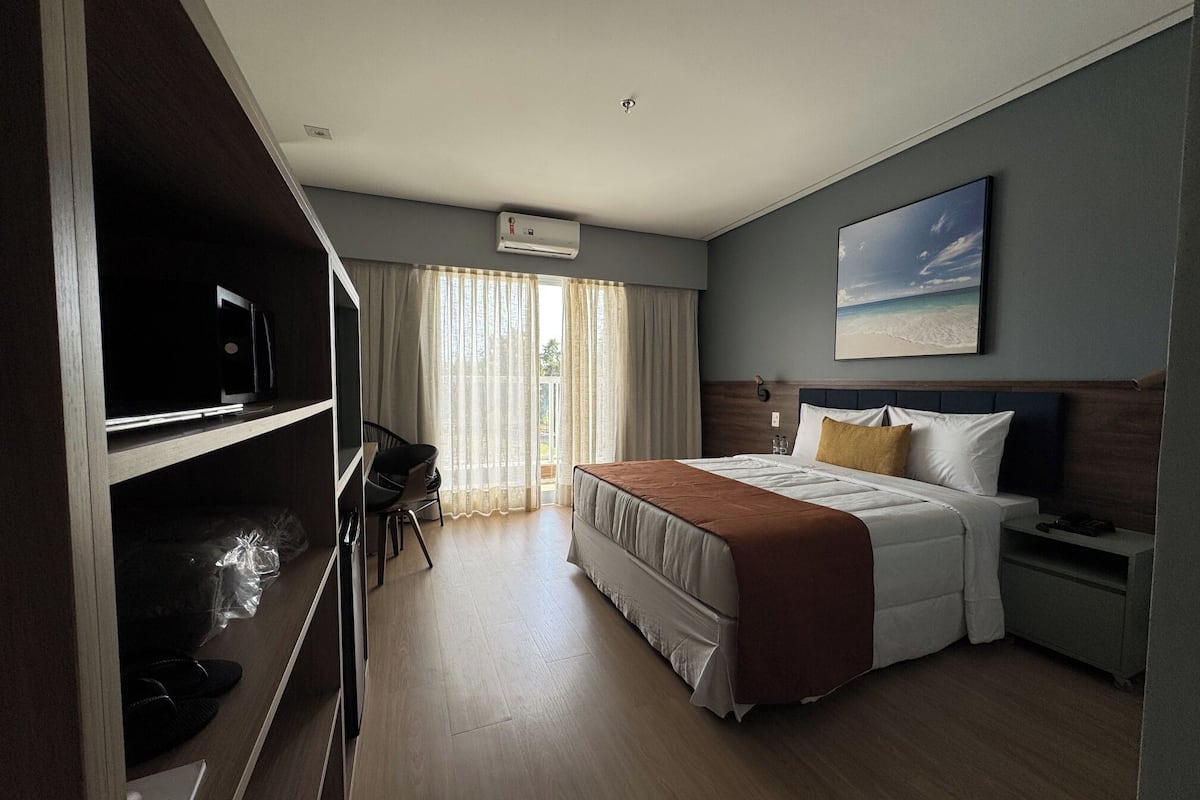 Una camera d'albergo con un letto, una scrivania, una sedia, una televisione e una finestra con tende.