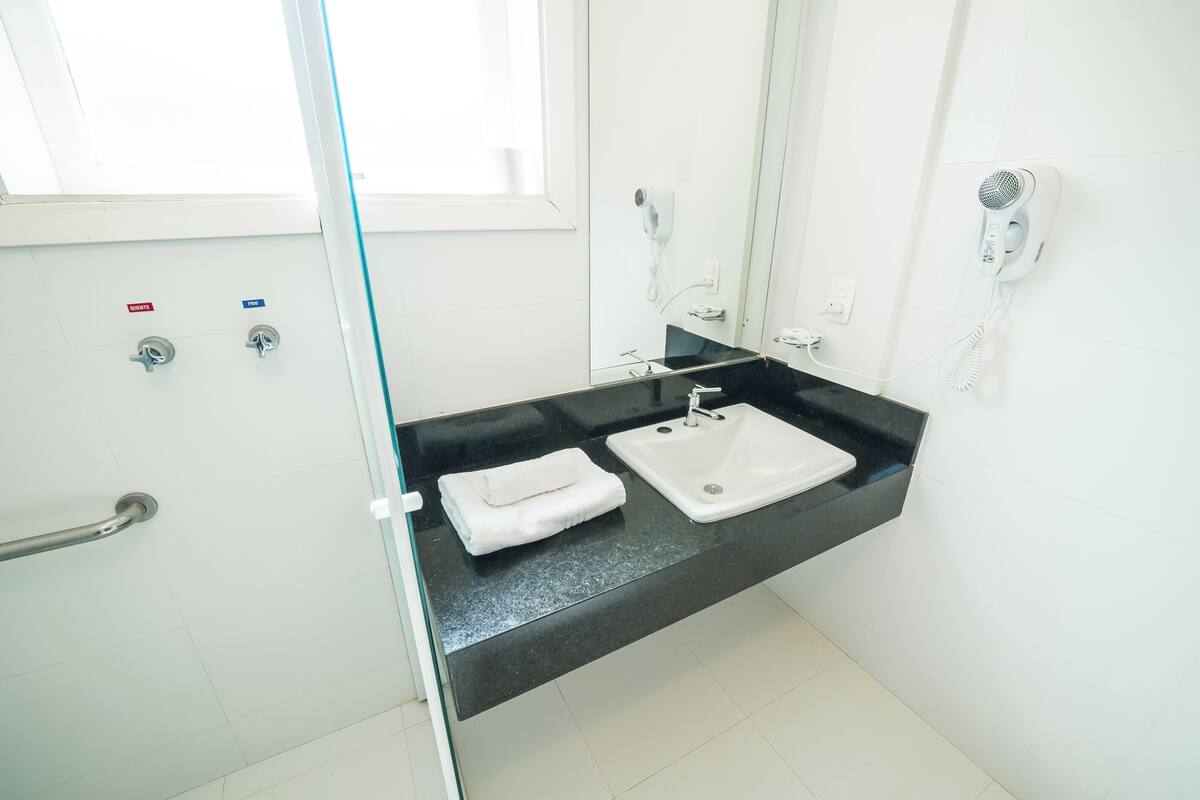 Un bagno con un piano di lavoro nero, un lavandino bianco, un asciugamano, un asciugacapelli e una cabina doccia in vetro.