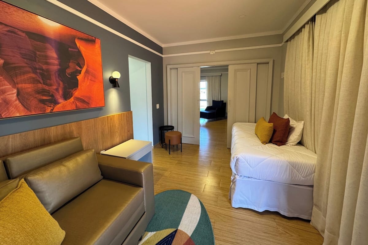 Una camera d'albergo con un quadro di grandi dimensioni, un divano, un letto con cuscini, un tavolino e una sedia.