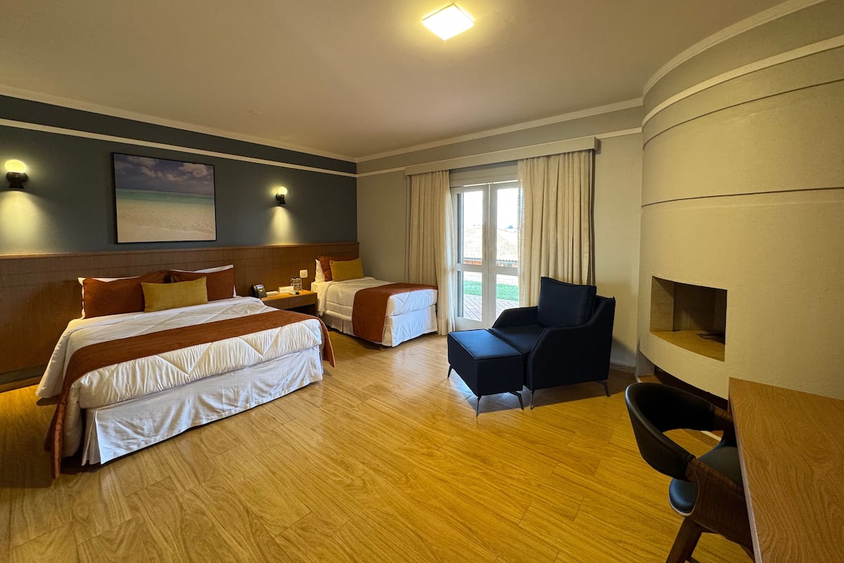 Camera d'albergo con due letti, un divano, una poltrona, un camino e un'ampia finestra con tende.