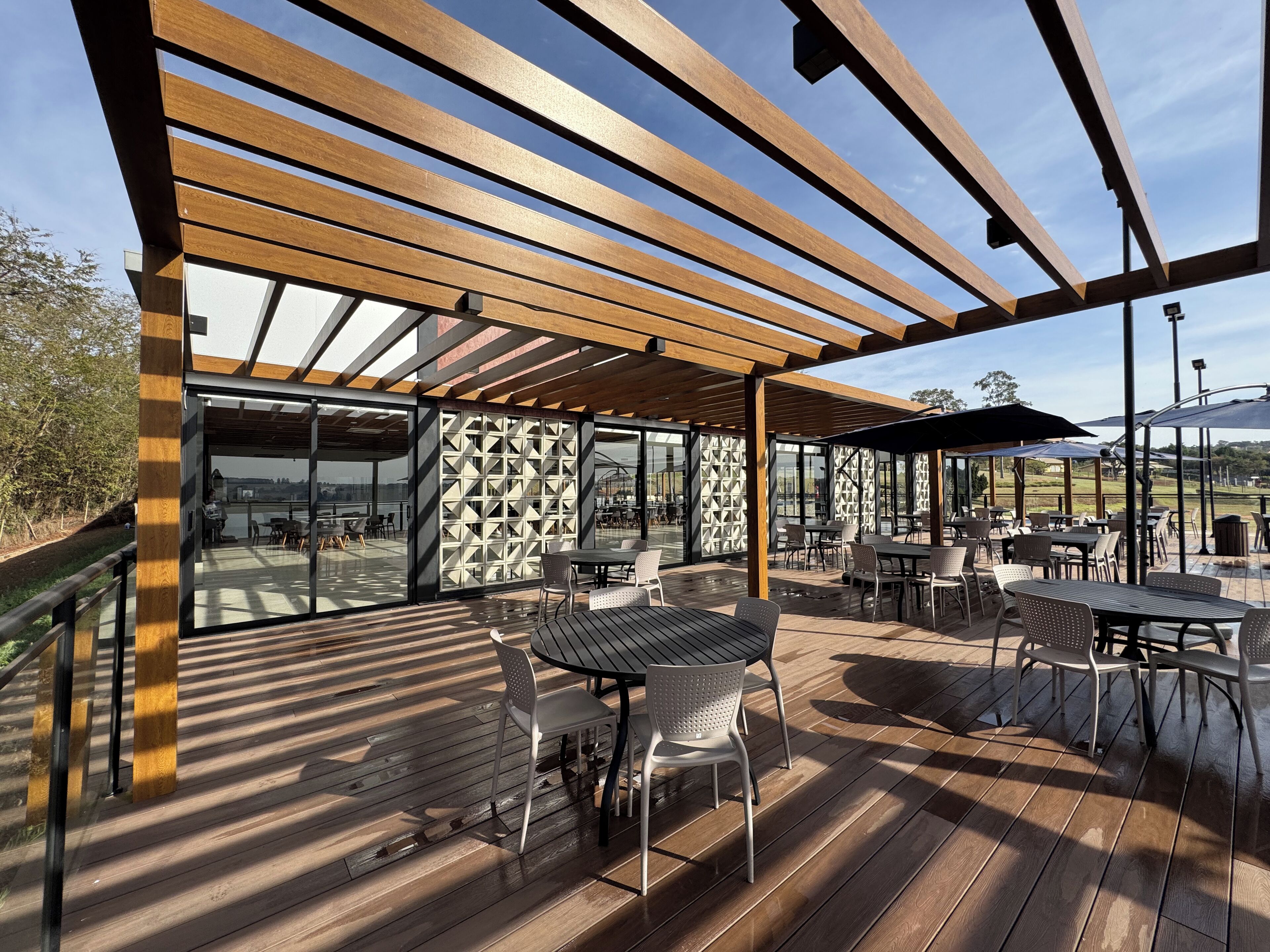 An outdoor patio with wooden flooring, tables, chairs, and umbrellas.
