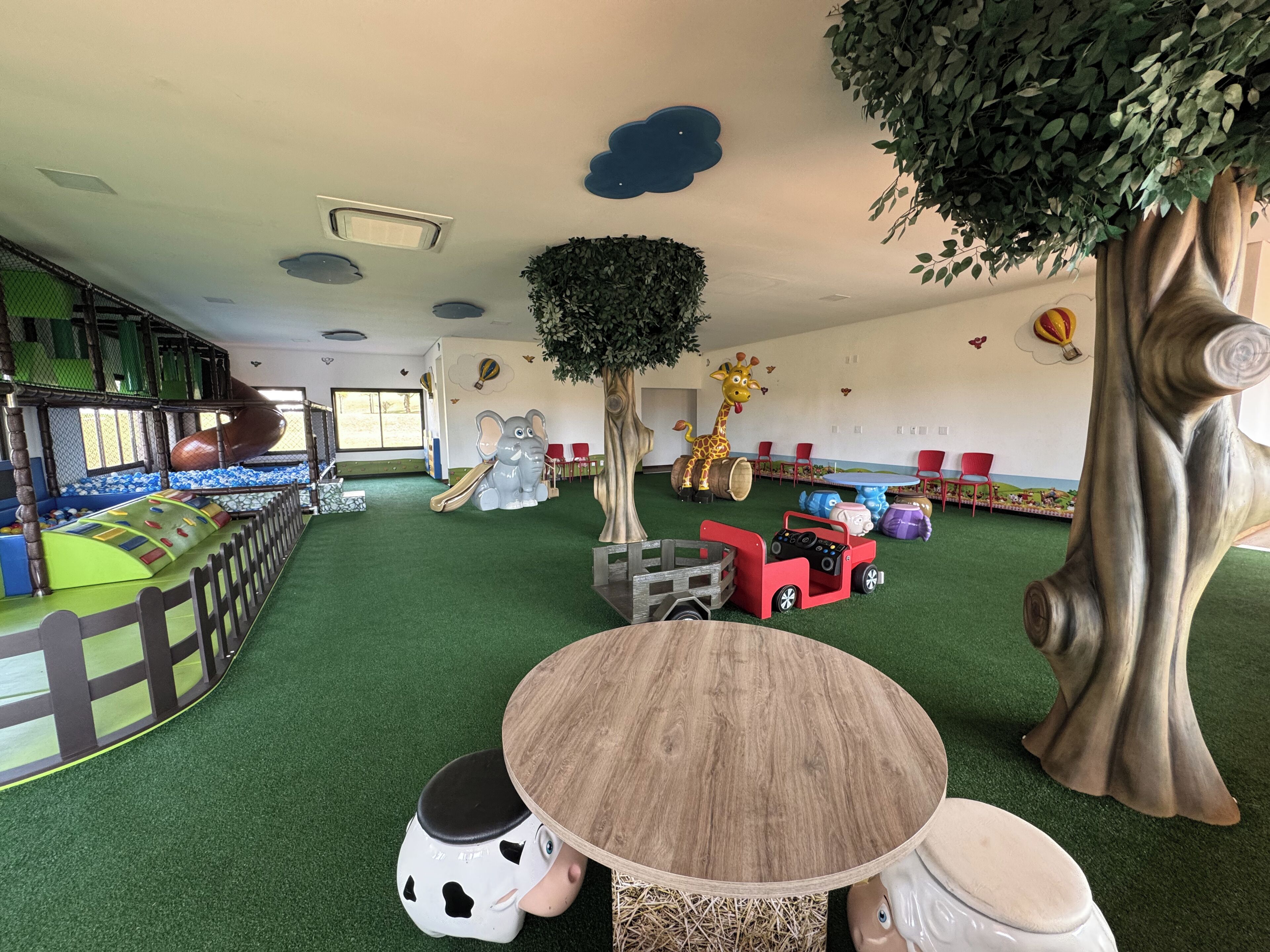 Zona de juegos infantiles con un tobogán, estructuras de juego y una gran decoración arbórea.