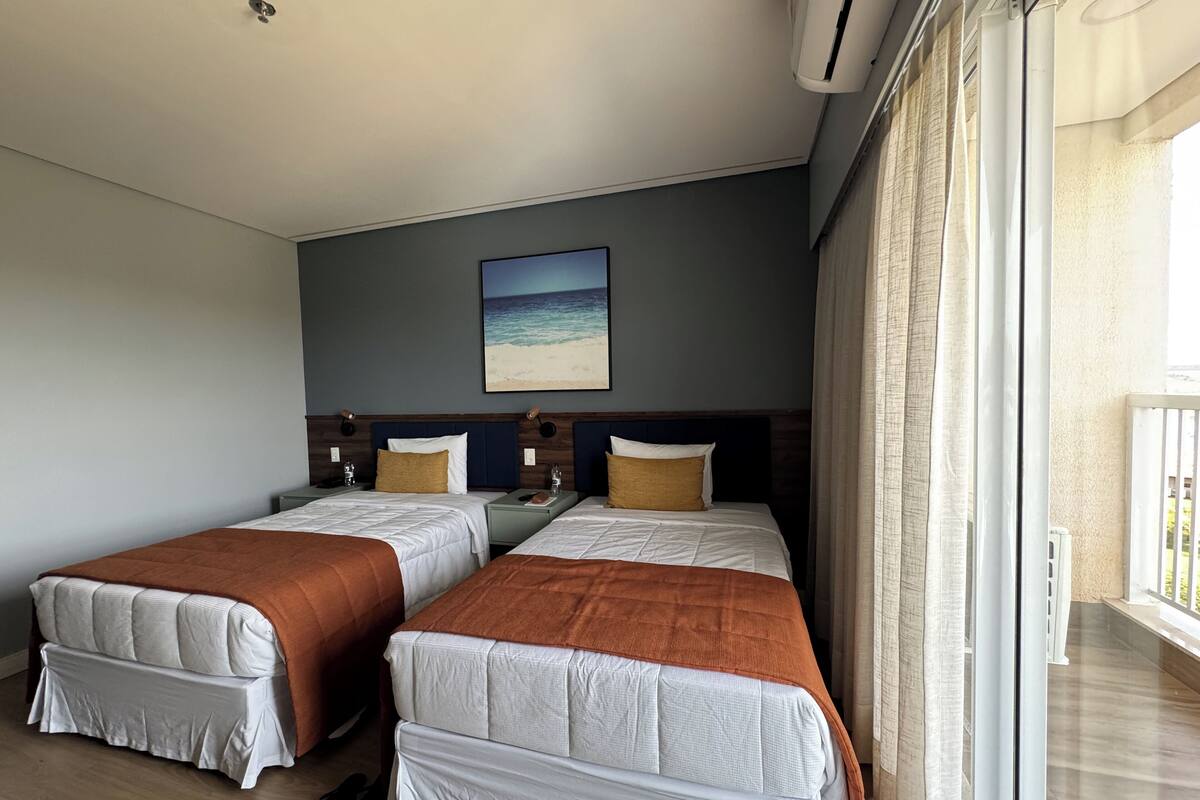 Camera d'albergo con due letti, un quadro raffigurante una spiaggia e un balcone con tende.