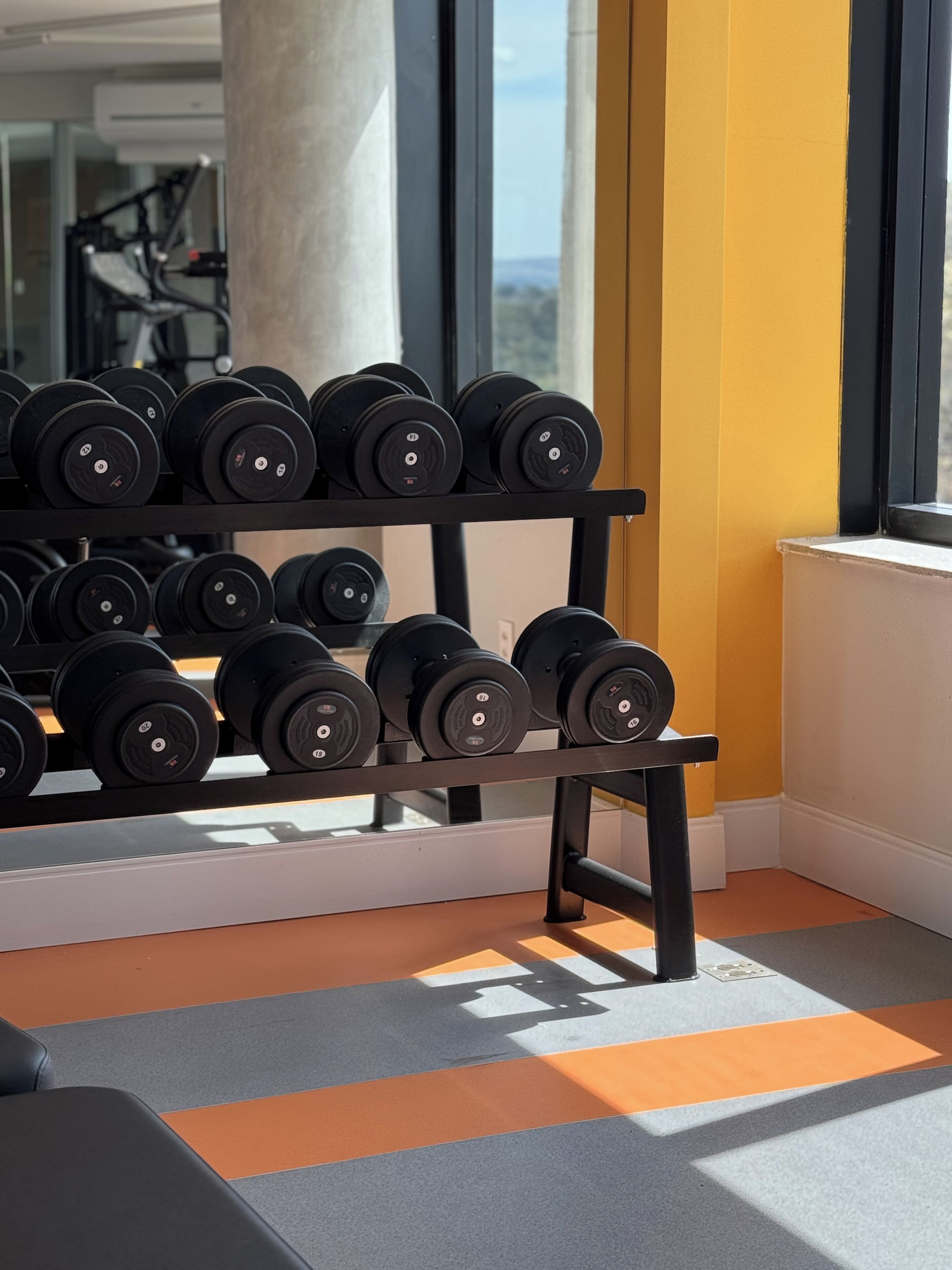 Un gimnasio con una barra de pesas, una ventana con vistas y un suelo de baldosas anaranjadas y grises.