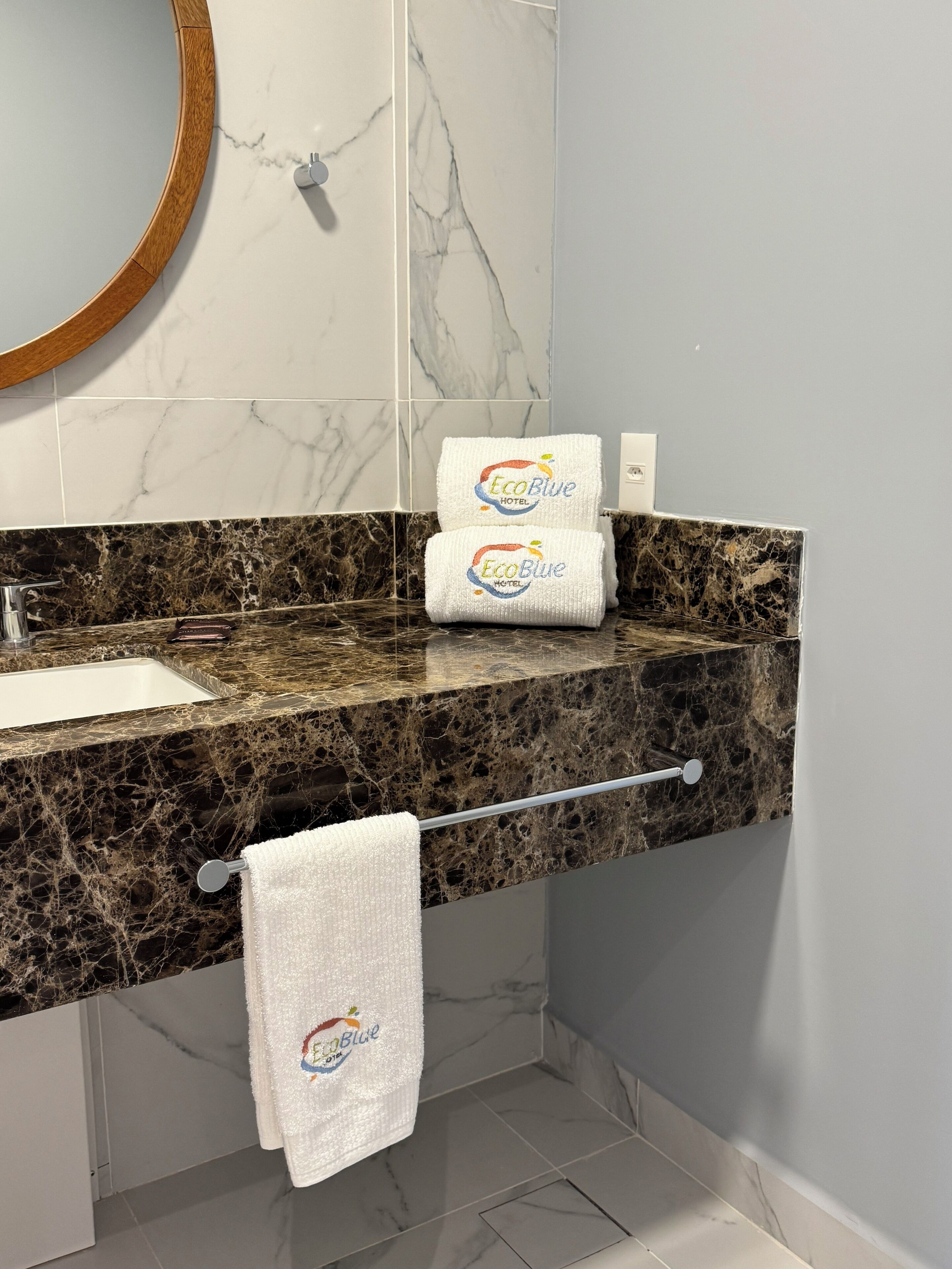 A bathroom with a marble countertop, a sink, and two folded towels with the EcoBlue Hotel logo.