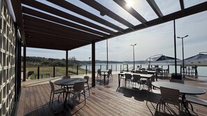 A covered outdoor patio with tables and chairs, overlooking a body of water and a golf course. - Ecoblue Resort Avaré (Avaré)