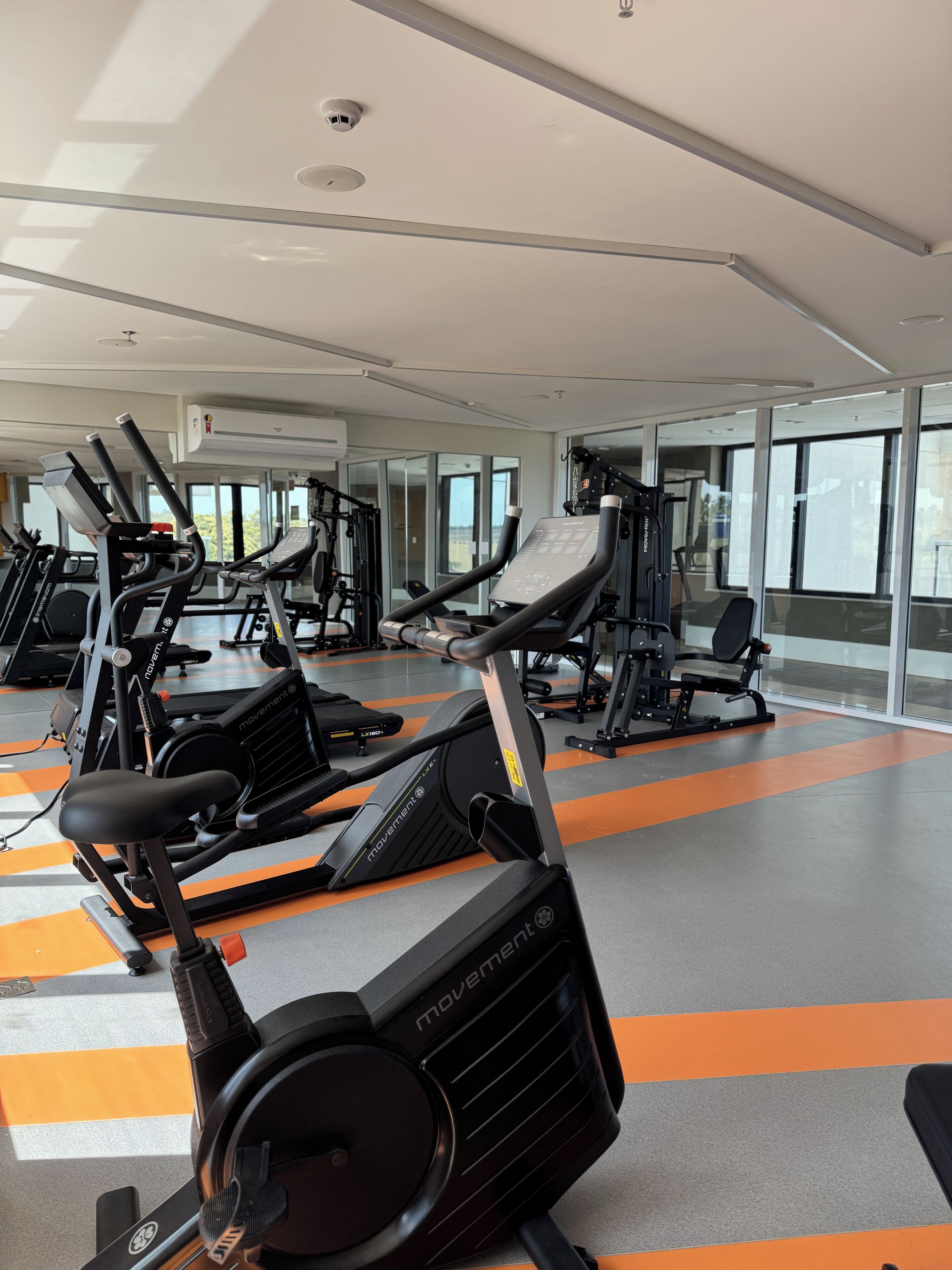 Un gimnasio con varias máquinas de ejercicio, ventanas amplias y un diseño moderno y limpio.