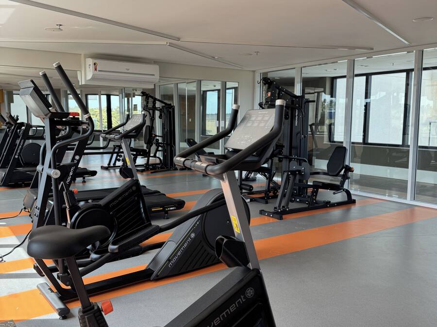 Un gimnasio con varias máquinas de ejercicio, ventanas amplias y un diseño moderno y limpio.