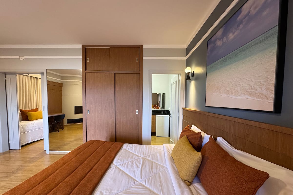 Camera d'albergo con un letto grande, una scrivania e un armadio. Si intravede la cucina e il bagno sullo sfondo.