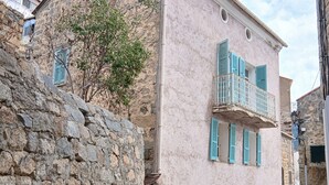 Una calle estrecha con muros de piedra y un edificio rosa con contraventanas azules.
