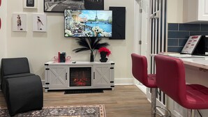 Un salon moderne avec une cheminée, un téléviseur fixé au mur et un coin repas avec des chaises rouges.