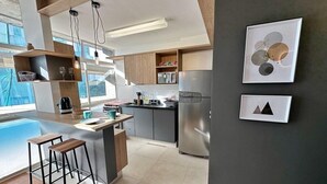 A modern kitchen with a central island, bar stools, and a large window providing natural light. - Vem pro Copan (São Paulo)