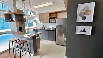 Een moderne keuken met een centraal eiland, barstoelen en een groot raam dat voor natuurlijk licht zorgt.