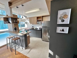 Uma cozinha moderna com uma ilha central, banquetas de bar e uma grande janela que oferece iluminação natural.