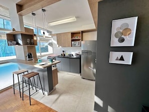 A modern kitchen with a central island, bar stools, and a large window providing natural light.