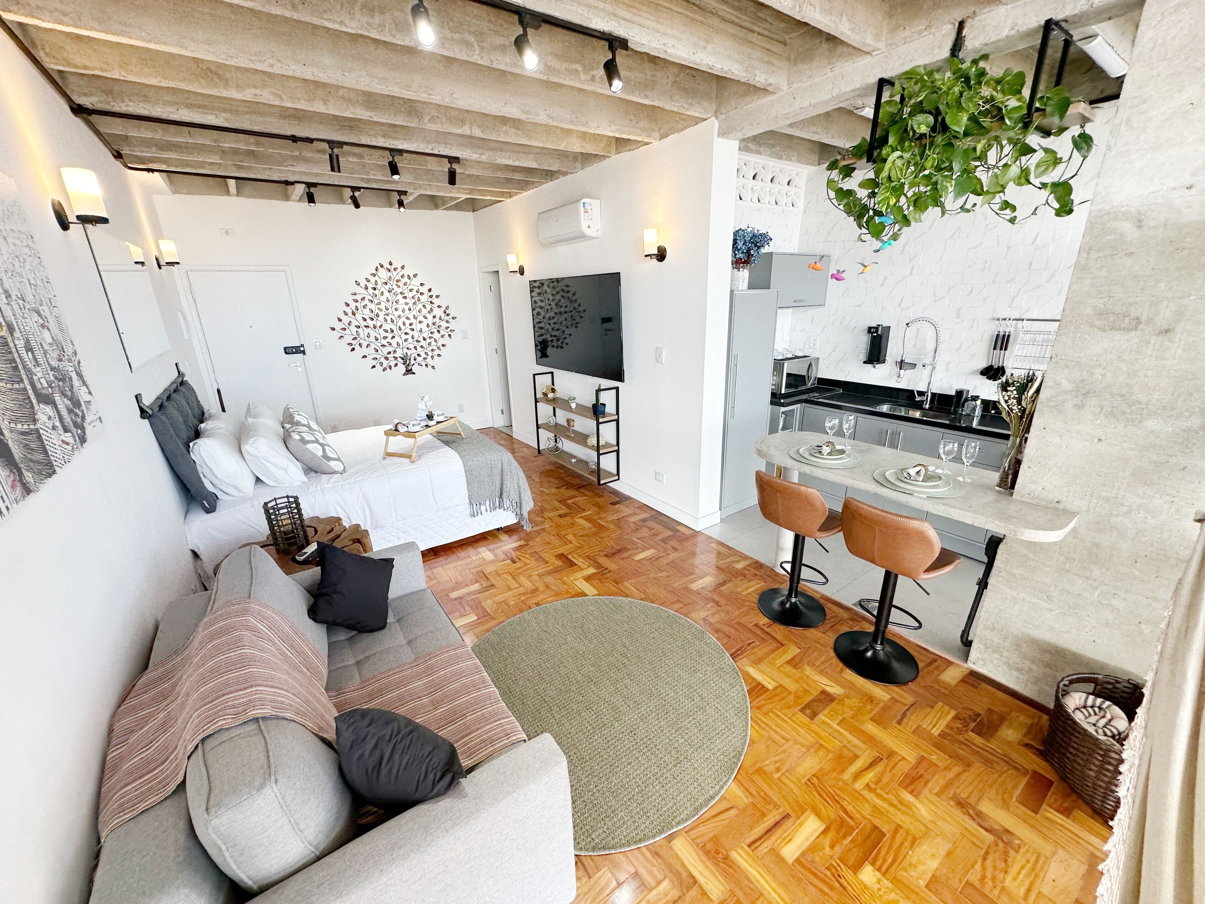 En moderne stue med sofa, et spiseområde med barstole, et køkken med mikroovn og et fjernsyn.