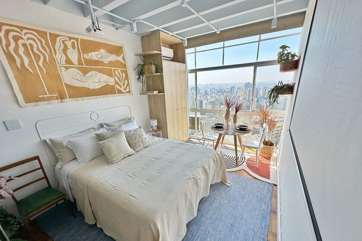 Une chambre avec un grand lit, une vue sur la ville et un balcon agrémenté de plantes.