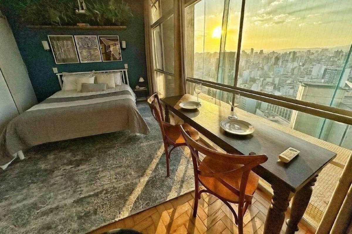 Une chambre avec un lit, une table à manger avec des chaises et une grande fenêtre donnant sur la ville.