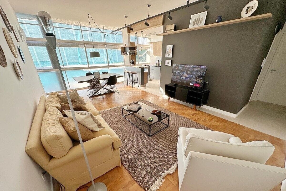 Un salon moderne avec un canapé, une table basse et un téléviseur. Au fond, on aperçoit une cuisine avec un coin repas.