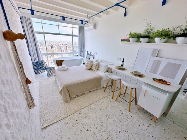 A modern bedroom with a bed, a desk, and a view of the city. - Vem pro Copan (São Paulo)