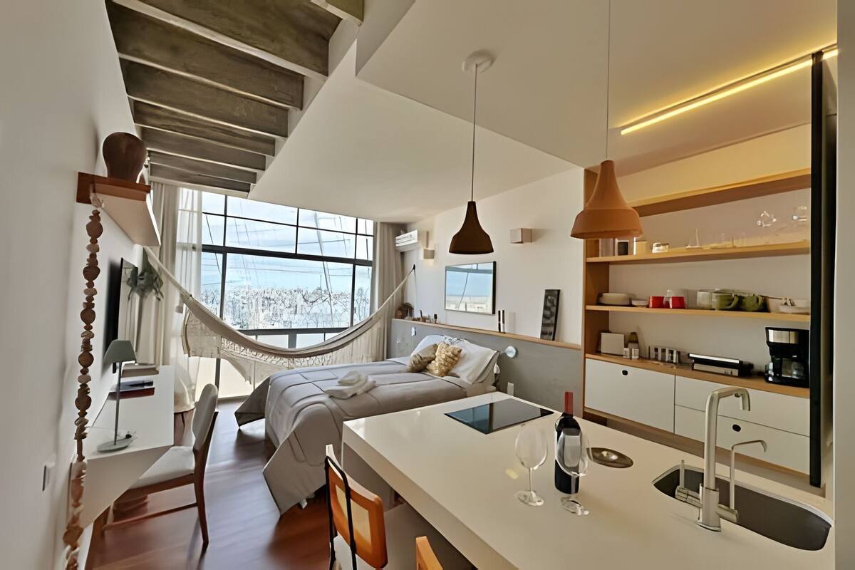 Une chambre moderne avec un hamac, une table de chevet, une lampe de chevet et une vue sur l’extérieur.