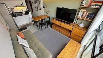A compact living space with a sofa, a dining table, a TV, and a bookshelf.