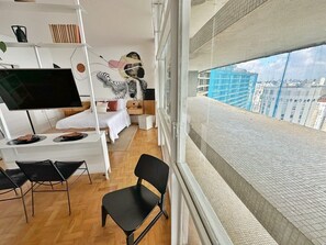 A modern room with a bed, a desk, and a large window overlooking a cityscape. - Vem pro Copan (São Paulo)