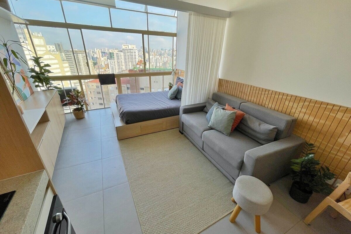 Un appartement moderne doté d’une grande fenêtre, d’un canapé gris, d’une petite table et d’un lit.
