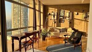 A spacious living room with a large window, a dining area, and a seating area with a sofa and armchairs. - Vem pro Copan (São Paulo)