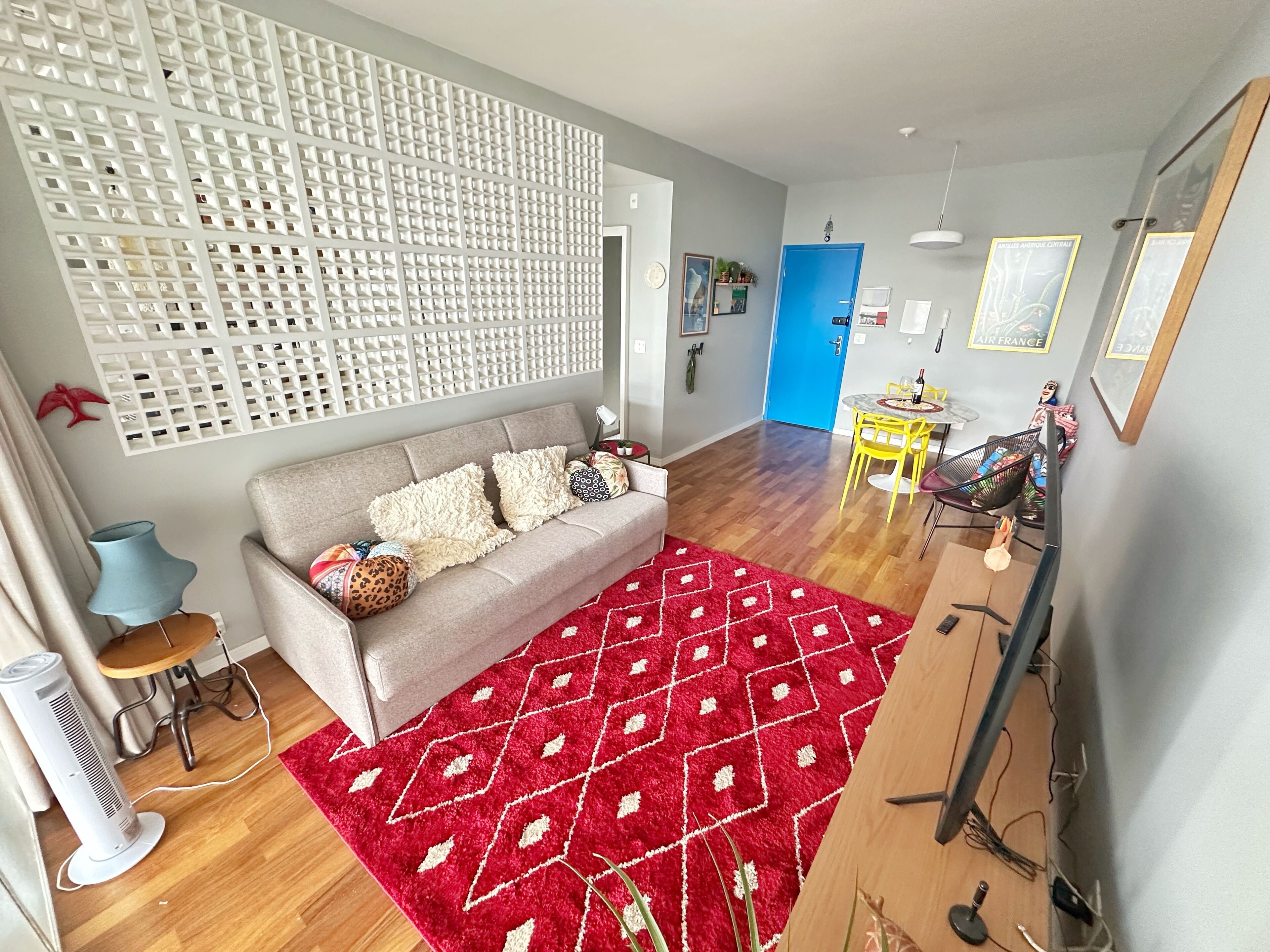 A living room with a grey sofa, red patterned rug, and a white partition wall.