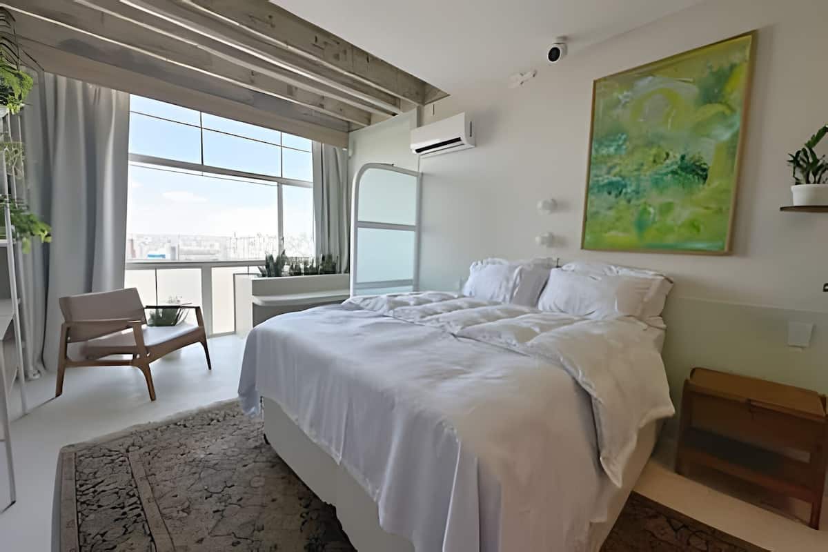 Une chambre moderne avec un grand lit, une vue sur la ville et un balcon agrémenté de plantes.