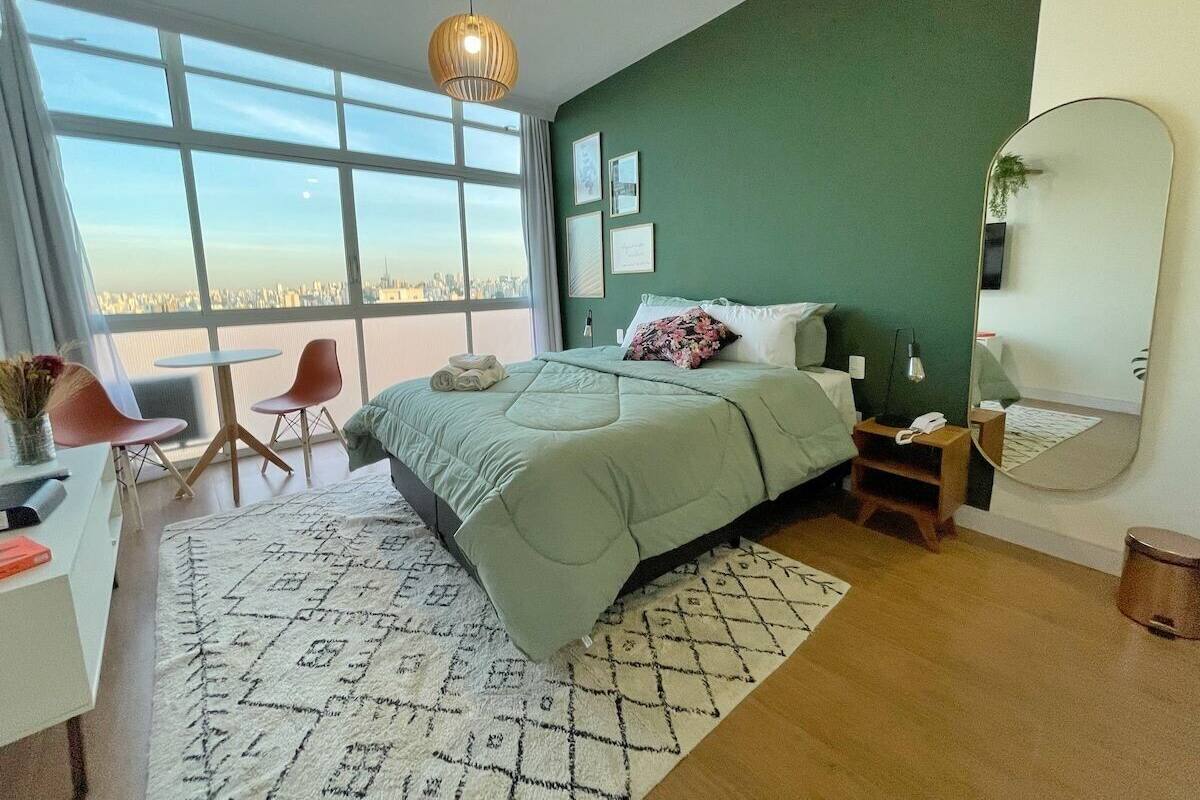 Une chambre moderne avec un grand lit, un bureau, deux chaises, une grande fenêtre et une vue sur la ville.