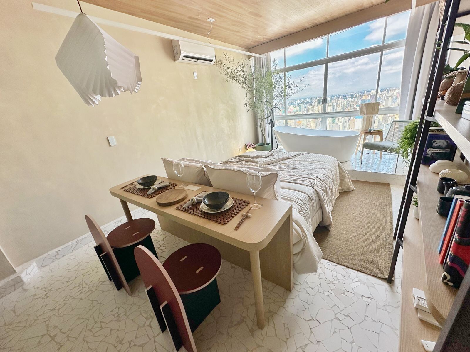 Ein modernes Schlafzimmer mit großem Fenster, einer Badewanne und einer Essecke mit Tisch und Stühlen.