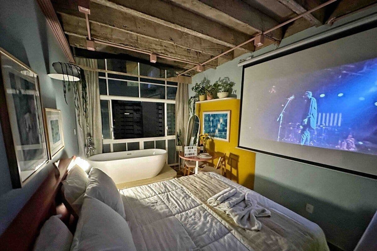 Une chambre avec un grand lit, une baignoire et un écran de télévision diffusant un concert.