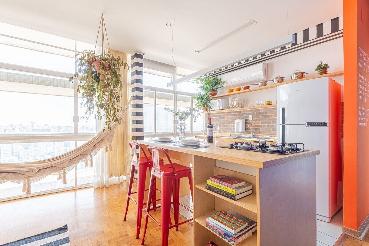 Een moderne keuken met een houten kookeiland, rode barstoelen en een hangplant.