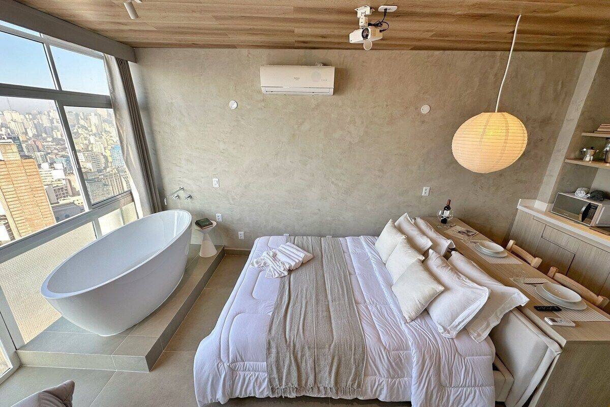 Une chambre moderne dotée d’une grande baignoire, d’un lit avec de nombreux oreillers et d’un coin repas offrant une vue sur la ville.